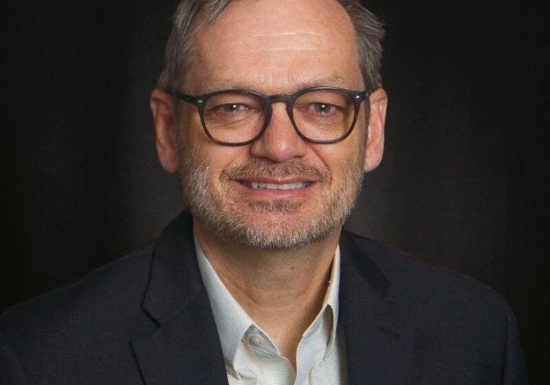 Man in suit and glasses smiling.